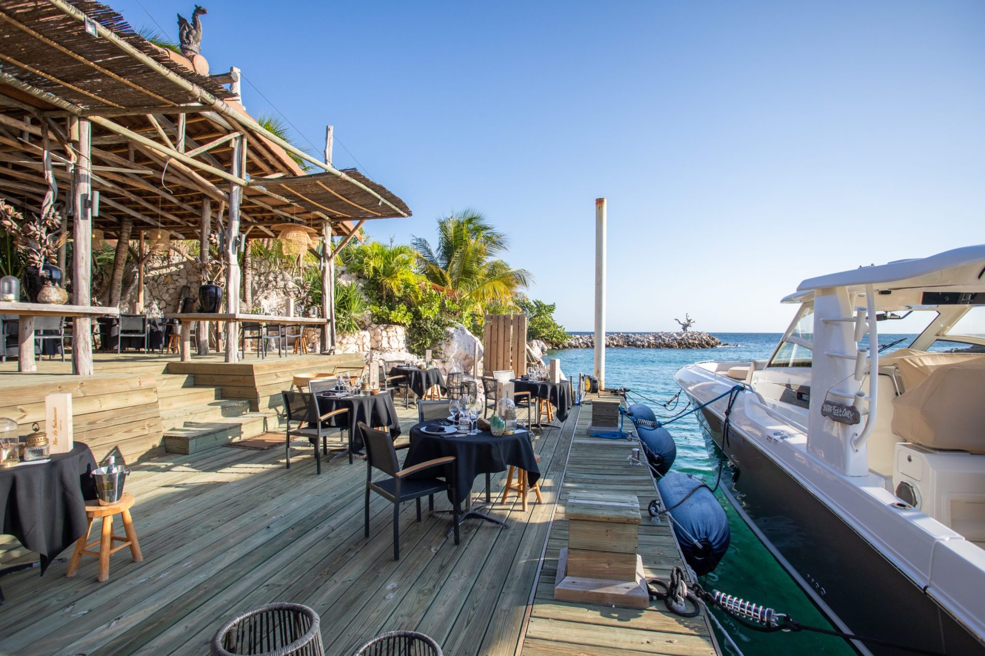Restaurant with tables set for dining next to a yacht in the sea